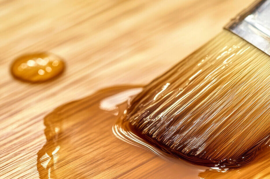 Varnishing a light wood surface with a brush, showcasing smooth strokes and clear resin drops on a rustic wooden table